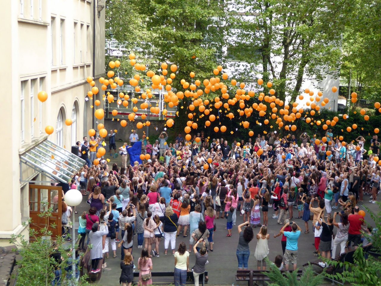 Auf einem Schulhof lassen dutzende Schülerinnen Luftballons in die Höhe steigen.