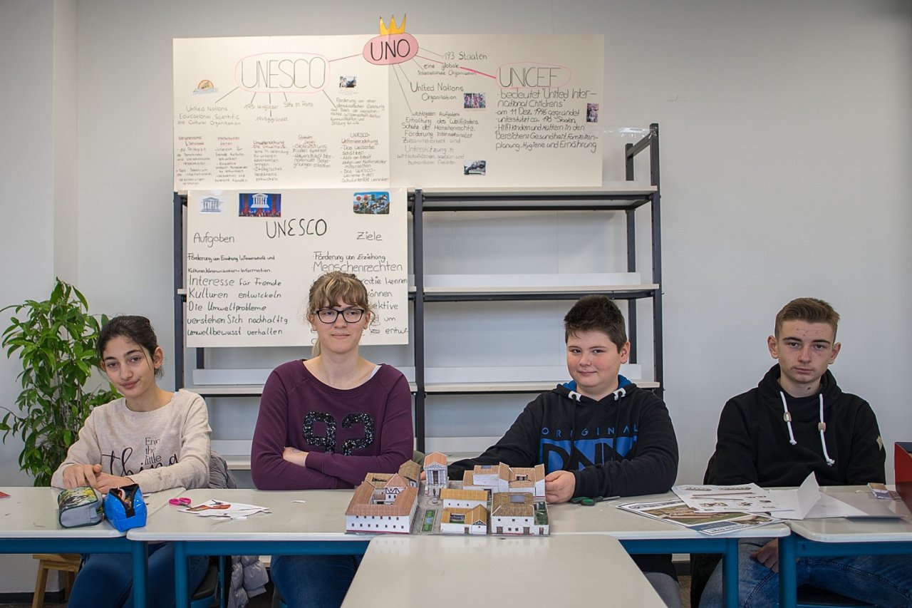 Schülerinnen und Schüler der UNESCO-AG der Heinrich Böll Schule sitzen vor selbst angefertigten Plakaten