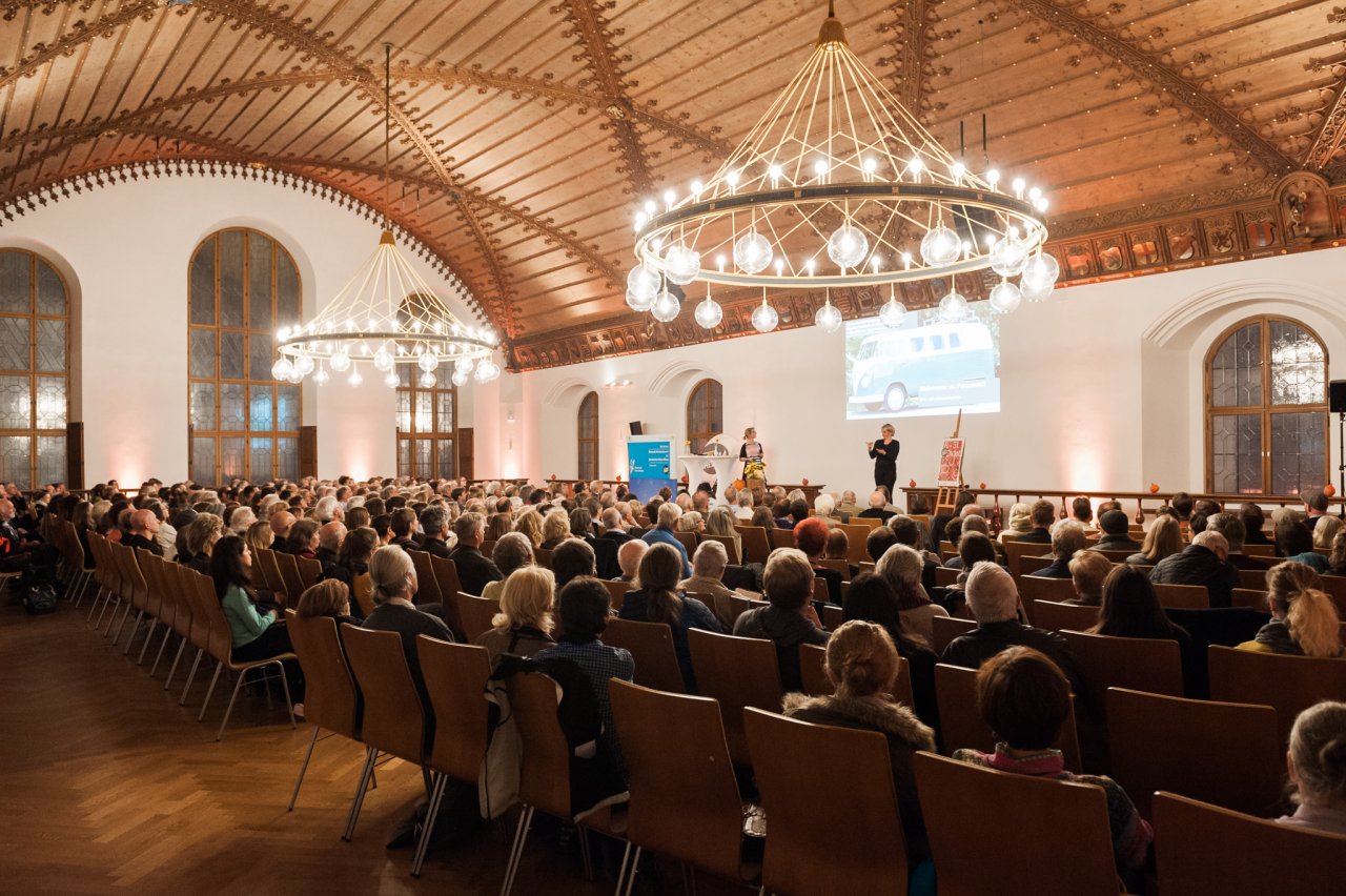 5 Menschen diskutieren auf einer Bühne vor einem Publikum.