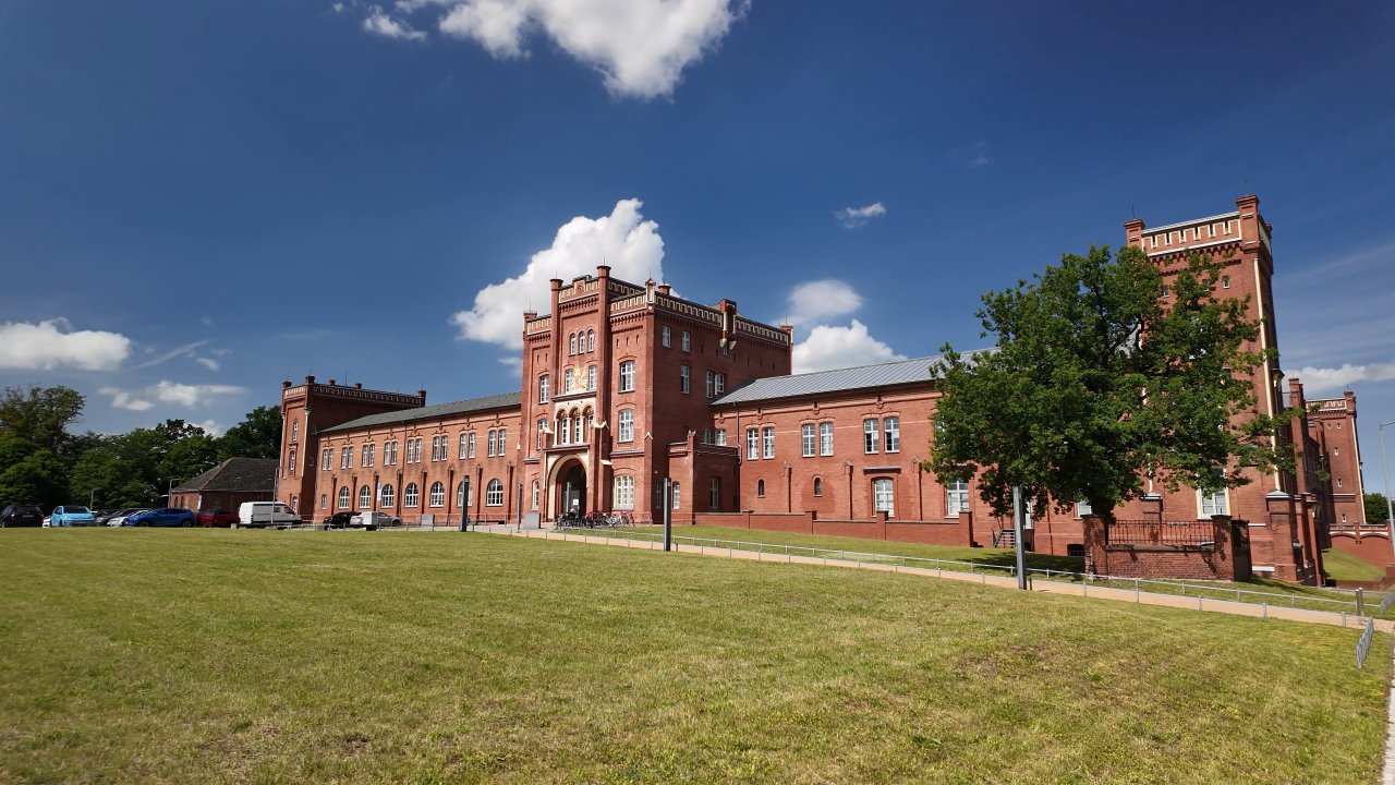 Fronansicht von der Alten Artilleriekaserne. Ein roter Backsteinbau im Historismus-Stil.