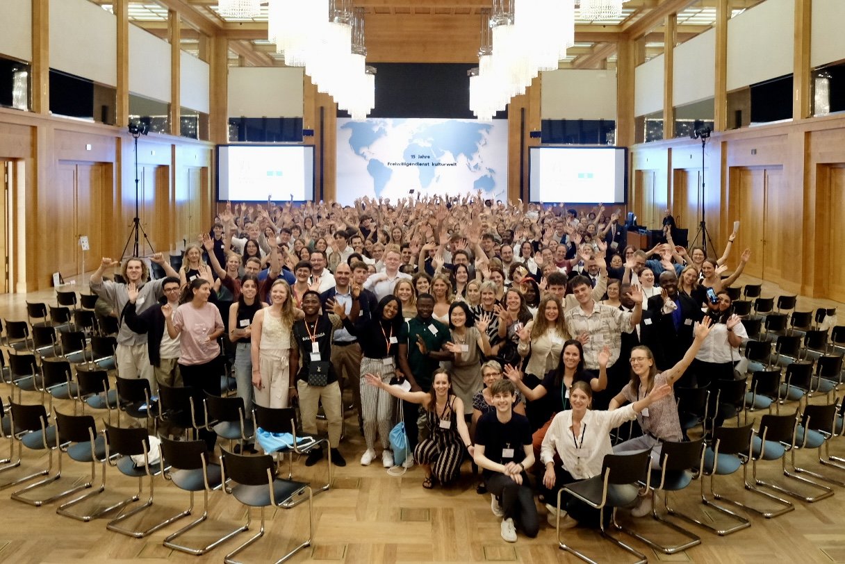 Eine Menschenmenge als Gruppenfoto in einem länglich geschnittenen Saal.