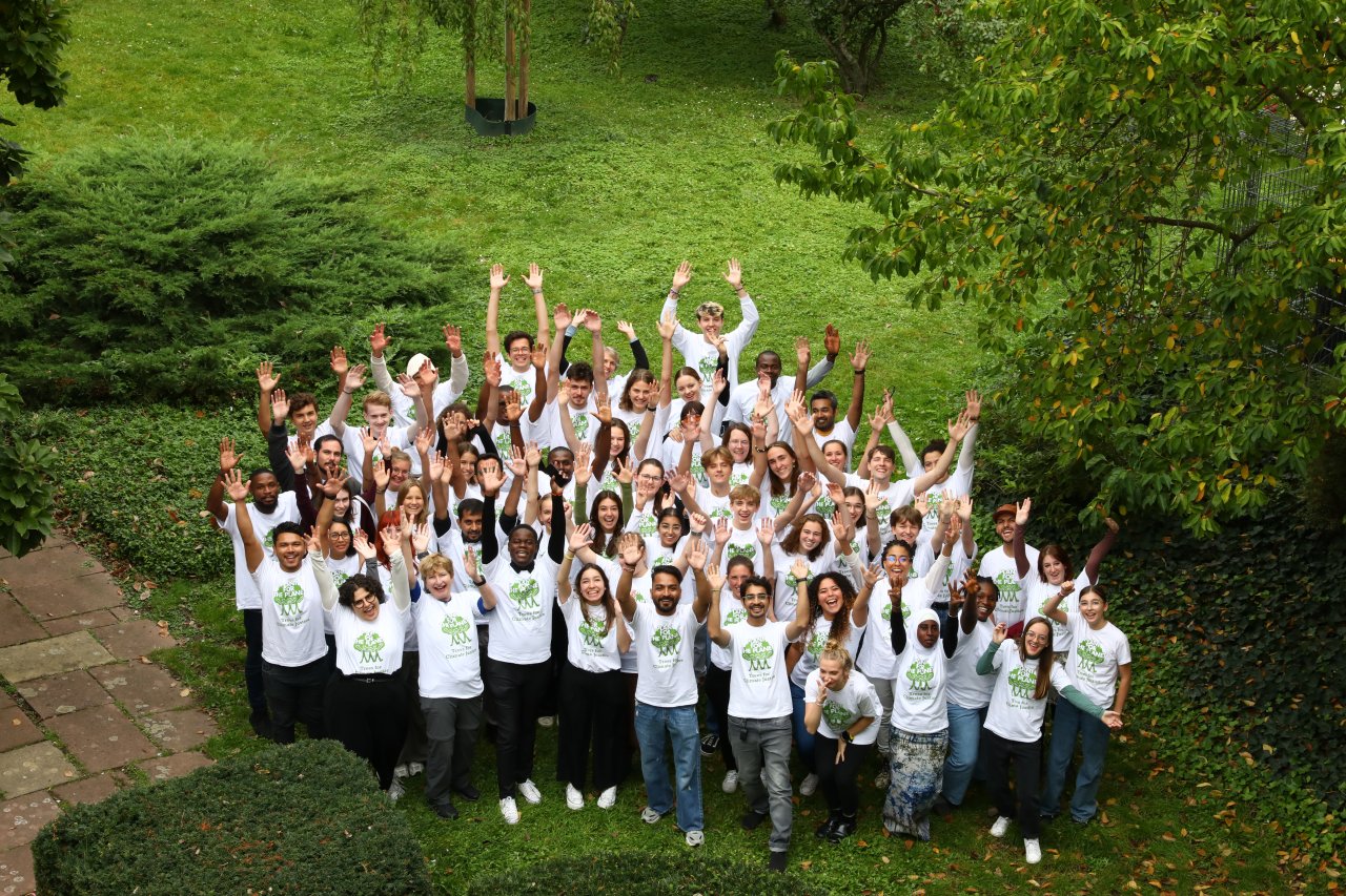 Eine Gruppe an Menschen mit erhobenen Händen vor einer Grünfläche.