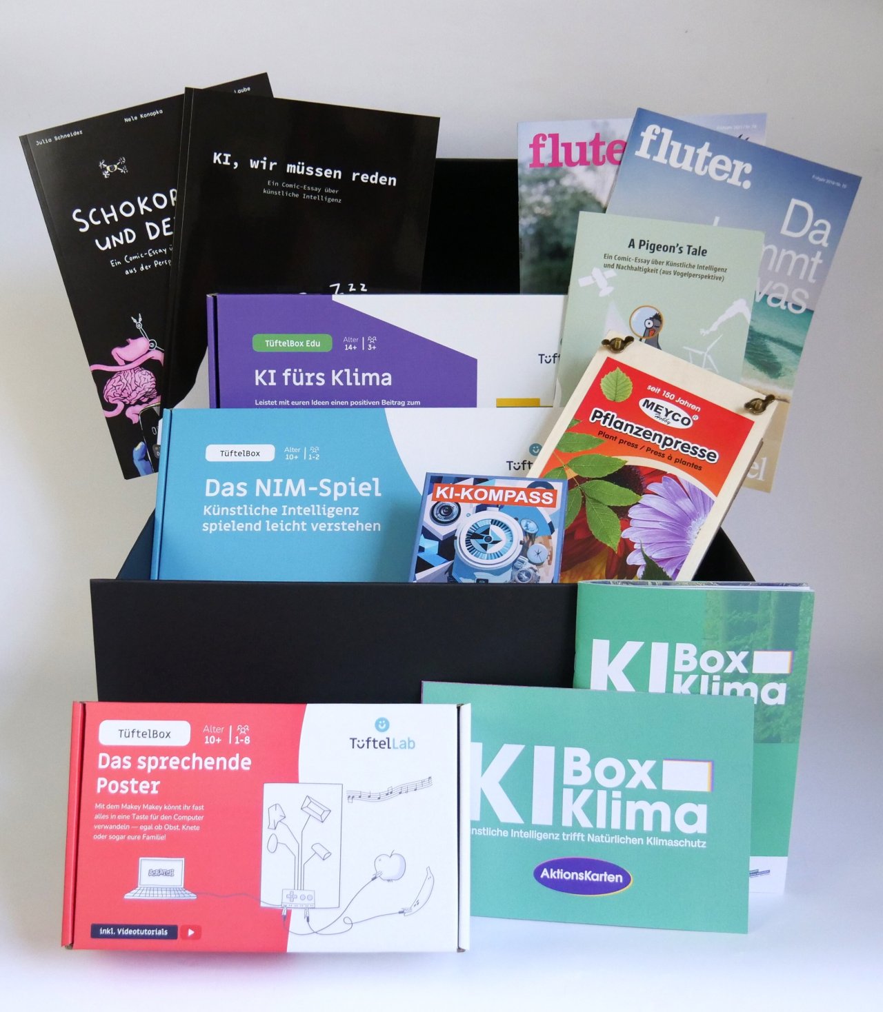 Eine Materialkiste mit unterschiedlichen Bildungsmaterialien: Spiele, Comics, Hefte und eine Pflanzenpresse.