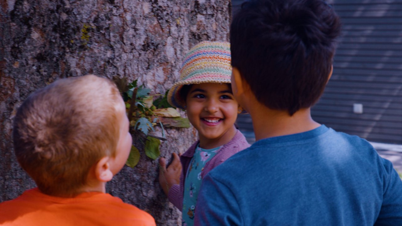 Drei Kinder stehen an einem Baum und freuen sich, dass er ein Gesicht hat