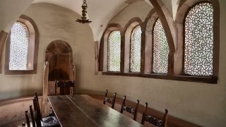 Das innere der Jeschiwa in Worms: ein langerdunkler Holztisch mit hölzernen Stühlen steht in einem Raum mit Fenstern aus gemustertem Glas.