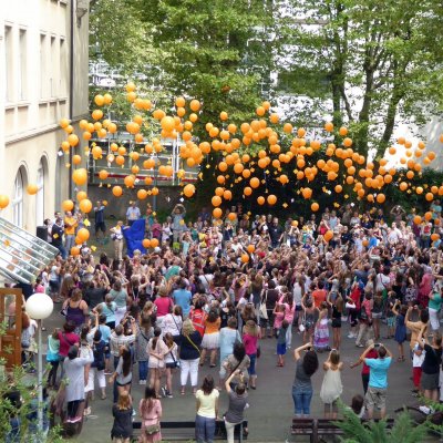 Auf einem Schulhof lassen dutzende Schülerinnen Luftballons in die Höhe steigen.