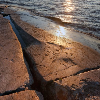 Felsbilder auf großen Steinen am Onegasee. Die Sonne spiegelt sich im Wasser.