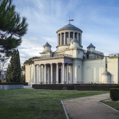 Das historische Gebäude des königlichen Observatoriums von Madrid steht in einem Park, es ist weiß und hat einige Säulen und Türme.