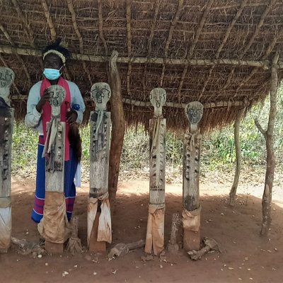 mehrere Personen unter einem einfachen Unterstand mit 5 Holzstatuen