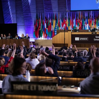 Zahlreiche Personen im Plenum der UNESCO-Generalkonferenz heben während einer Abstimmung ihre Hände.